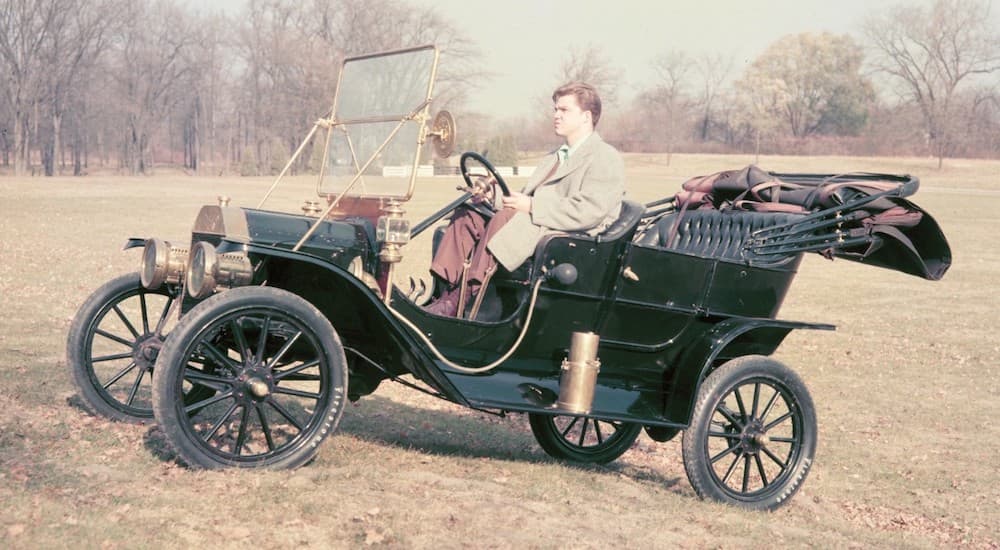 A green 1908 Ford Model T is shown driving on a hill.