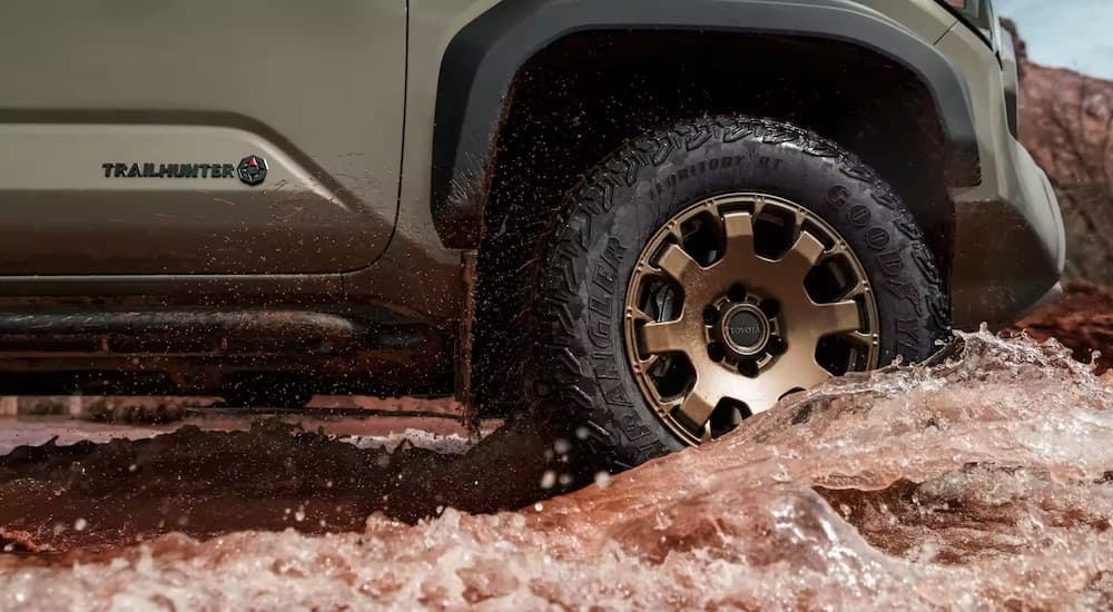 A green 2024 Toyota Tacoma Trailhunter is shown driving through muddy water at a low angle.