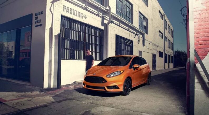 An orange 2019 Ford Fiesta St is shown parked on a corner of a city street.