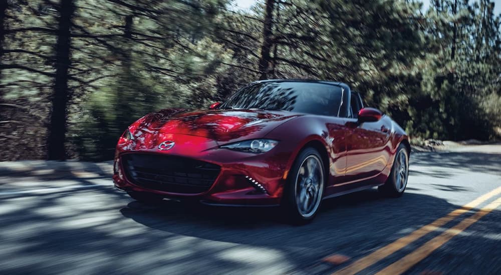 A red 2021 Mazda MX-5 Miata is shown driving on a highway after viewing used cars for sale.