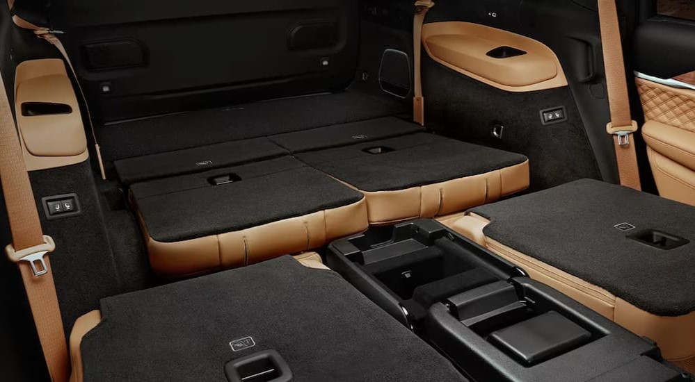 The black and tan interior cargo space of a 2023 Jeep Grand Cherokee L is shown with the seats folded down.