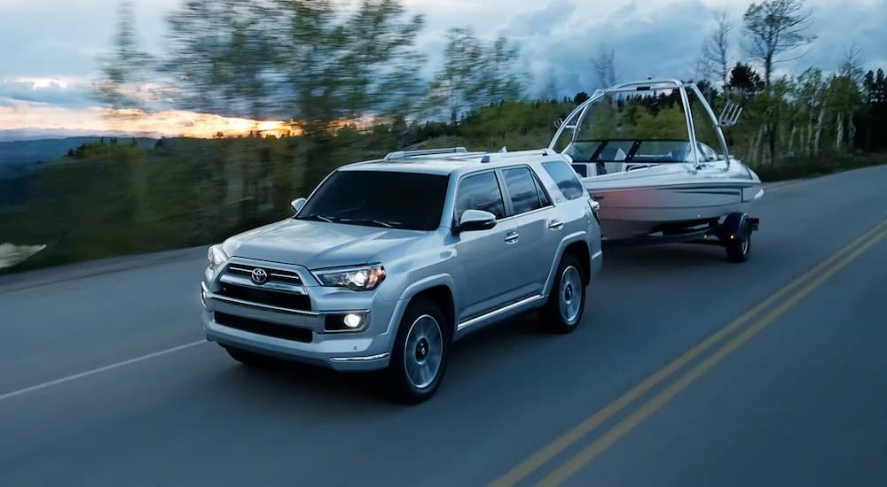 A silver 2023 Toyota 4Runer is shown towing a boat on a highway.