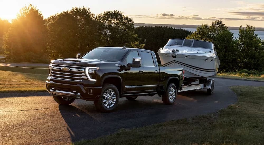 A black 2024 Chevy Silverado 3500 HD High Country is shown towing a boat.