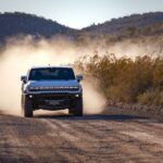 A white 2024 GMC Hummer EV is shown on a dusty path after leaving a GMC dealer.