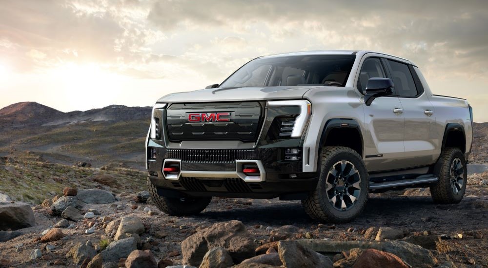 A white 2025 GMC Sierra EV AT4 is shown parked on rocks.