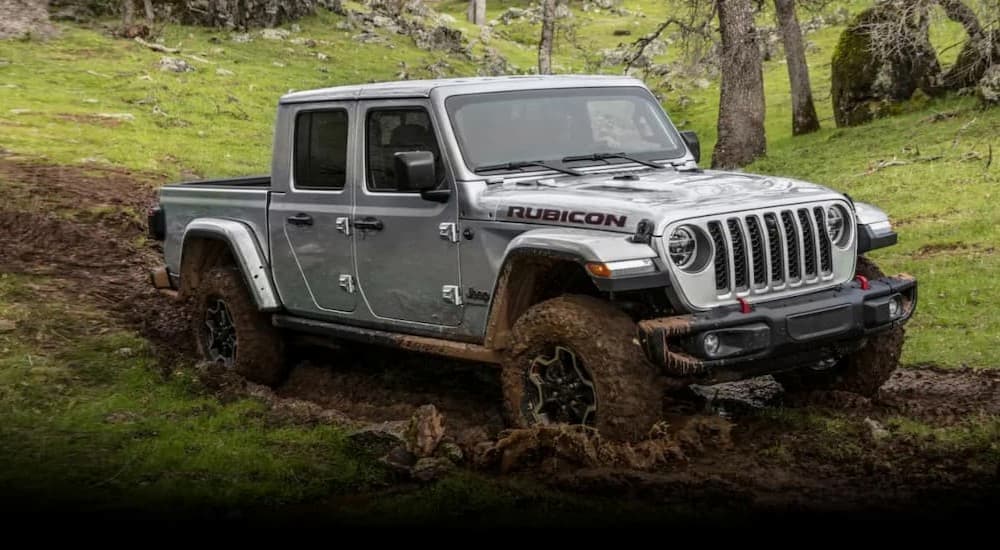 A silver 2023 Jeep Gladiator Rubicon is shown driving off-road on mud.