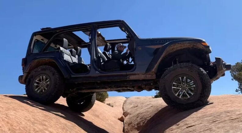 A dark gray 2024 Jeep Wrangler Rubicon is shown driving over a gap after visiting a Jeep dealer.