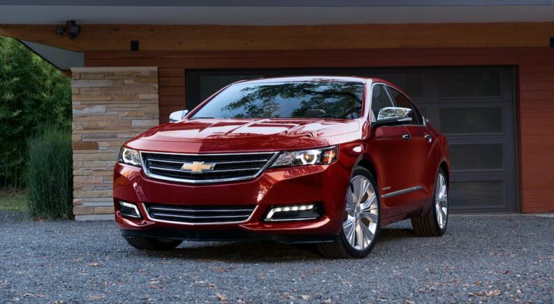 A red 2020 Chevy Impala is shown parked near a garage after visiting a Chevy dealer.