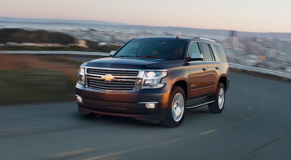 A brown 2020 Chevy Tahoe is shown driving with a cityscape in the background.
