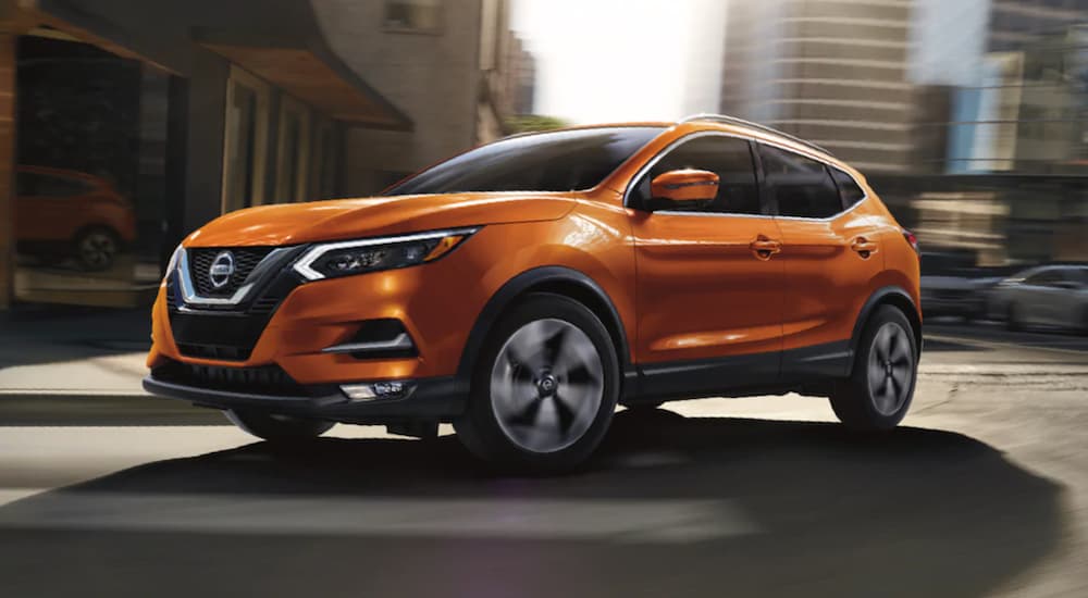 An orange 2020 Nissan Rogue Sport is shown parked in a cityscape.