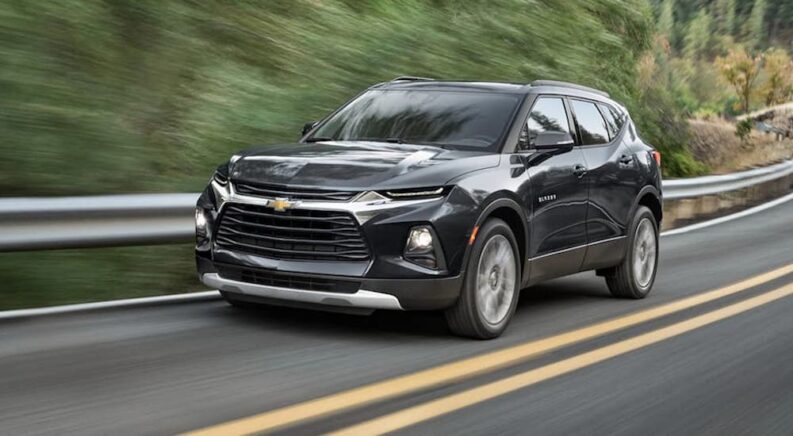 One of the most common used Chevy SUVs for sale, a black 2021 Chevy Blazer, is shown driving through a forest road.