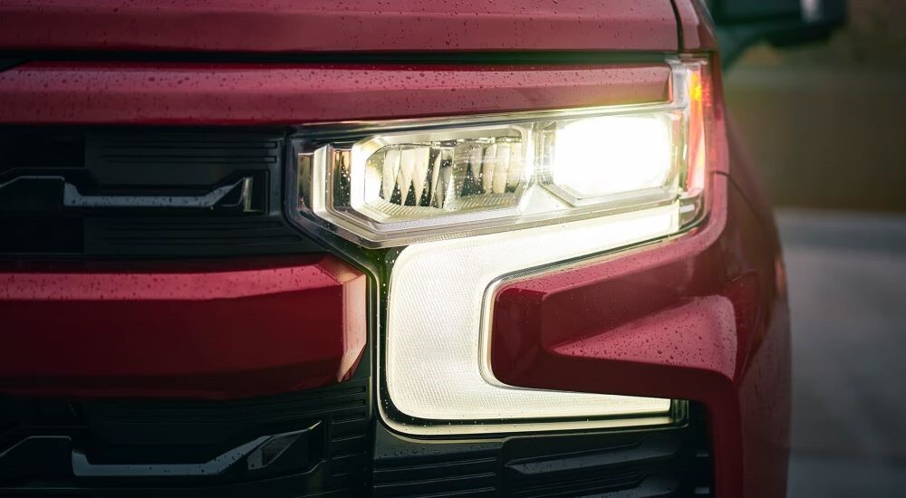A close-up shows the driver-side headlight of a red 2023 Chevy Silverado 1500 RST.