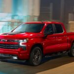 A red 2023 Chevy Silverado 1500 RST is shown driving on a city street at night.