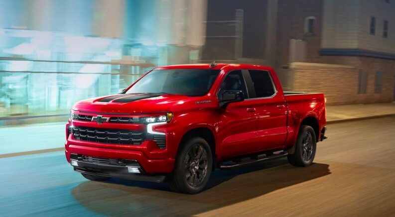 A red 2023 Chevy Silverado 1500 RST is shown driving on a city street at night.