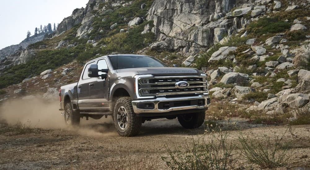 A gray 2023 Ford F-250 Tremor is shown driving off-road near a mountain.