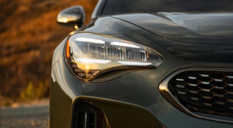 A close-up on the headlight of a grey 2023 Kia Stinger as it drives away from a Northampton Kia dealer.