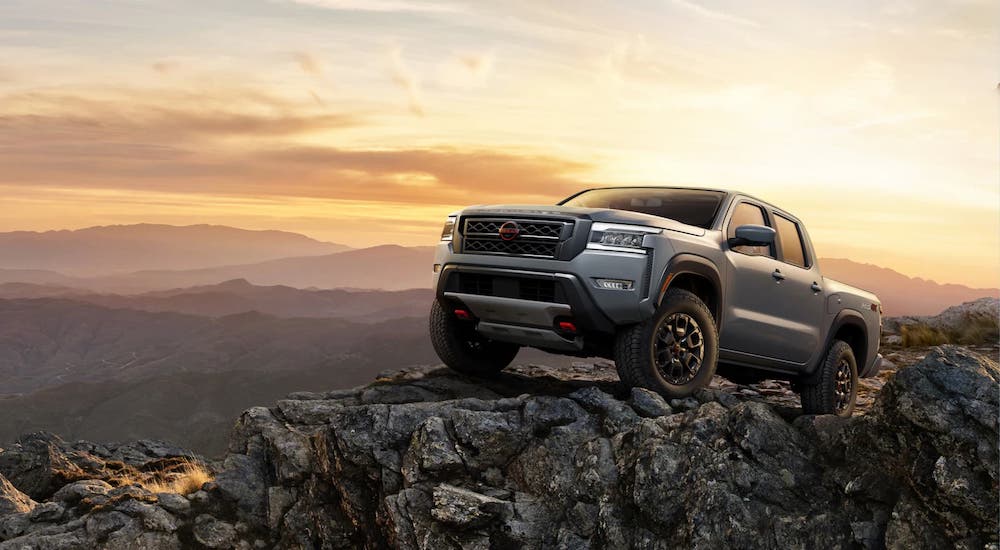 A silver 2023 Nissan Frontier is shown parked off-road atop a rocky cliff.