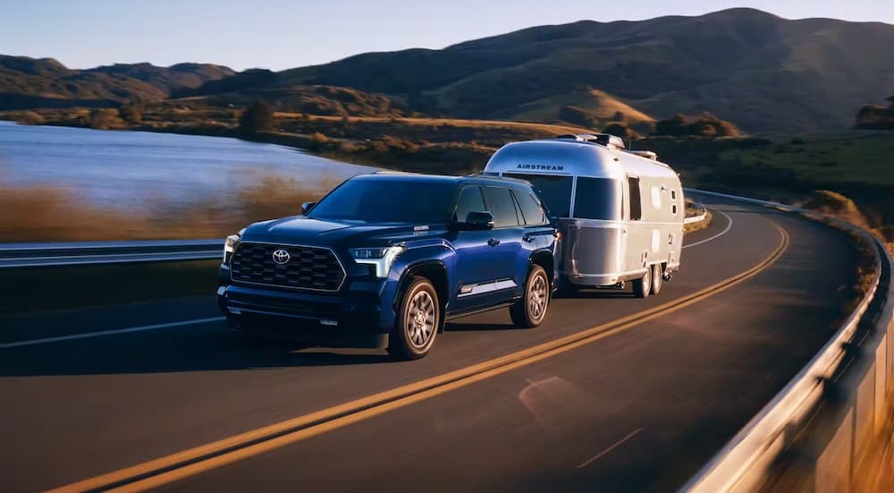 A blue 2023 Toyota Sequoia is shown towing a trailer near a lake.