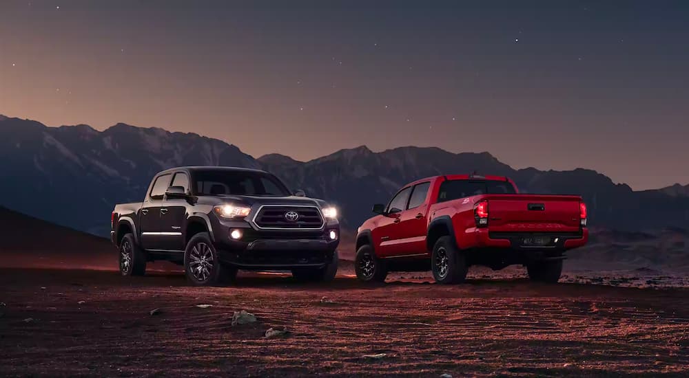 A pair of 2023 Toyota Tacoma SR5, one red and the other black, are shown parked off-road.