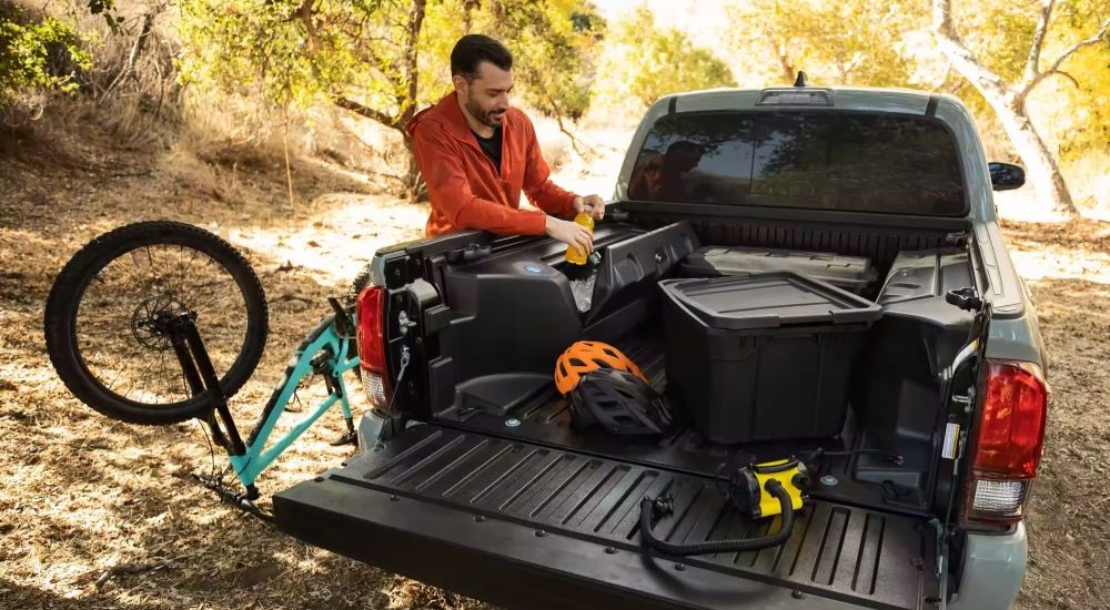 A man is shown unloading a bike from the bed of a black 2023 Toyota Tacoma SR5 Trail Edition.