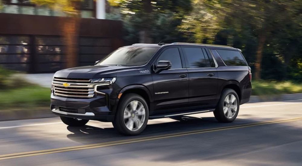 A black 2023 Chevy Suburban High Country is shown driving on a street after viewing used SUVs for sale.