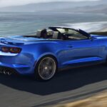 A blue 2024 Chevy Camaro is shown driving near the ocean.