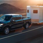 A black 2024 Chevy Silverado 1500 ZR2 hauling a trailer away from a Chevy Silverado dealership.