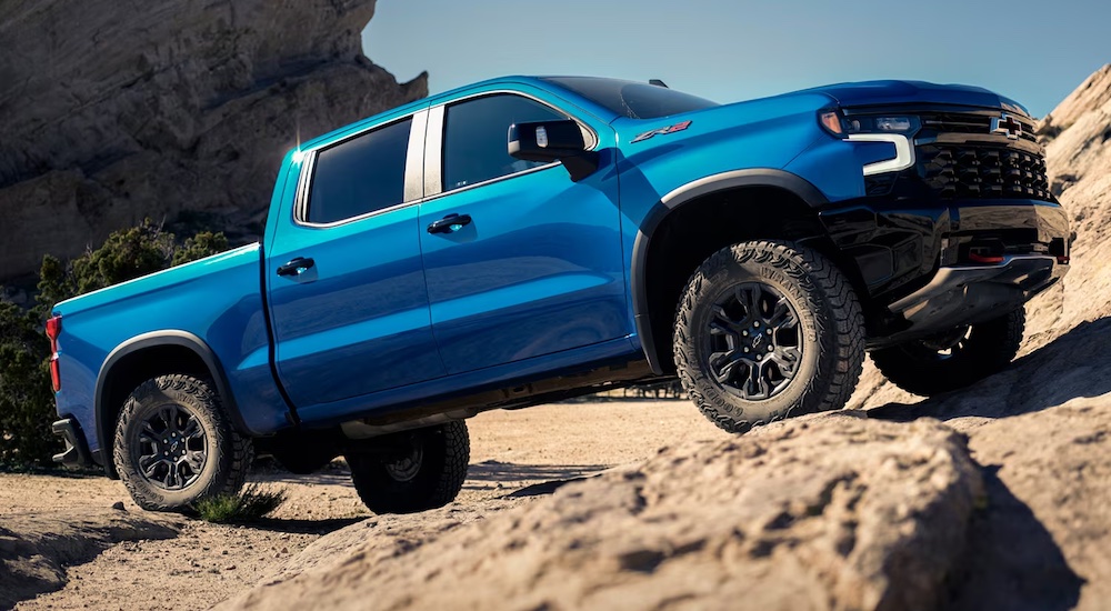 A blue 2024 Chevy Silverado 1500 ZR2 driving off-road up a sandy hill.