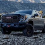 A grey 2024 GMC Sierra 1500 is shown driving up a rocky mountain road.