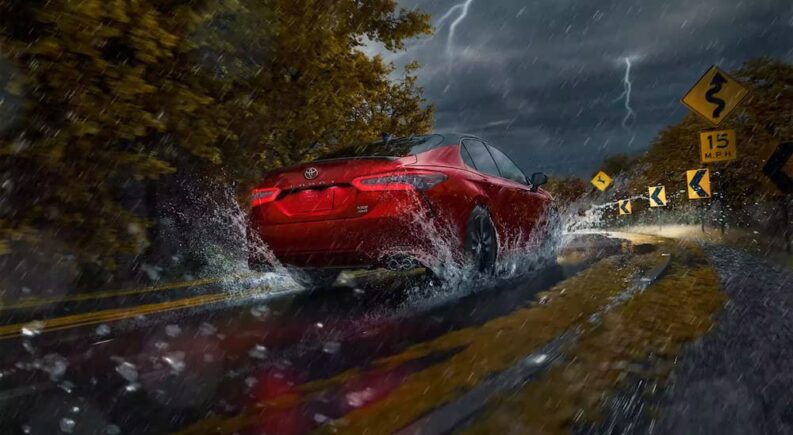 A red 2024 Toyota Camry is shown driving through a storm.