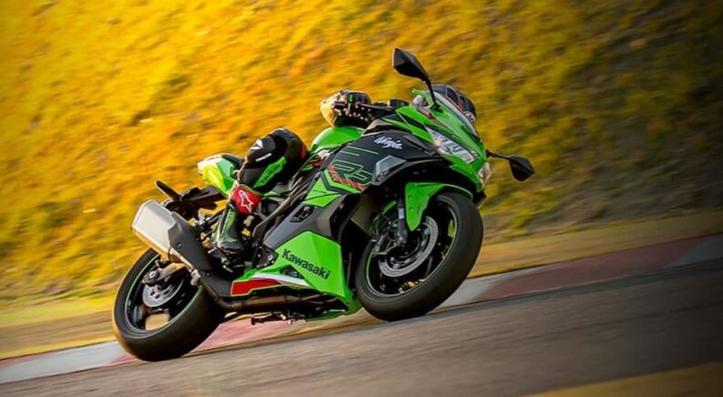 One of the more popular Japanese 400cc class motorcycles, a green 2023 Kawasaki Ninja ZX-4RR KRT Edition, is shown driving on a racetrack.