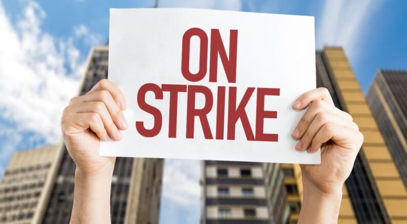 A close up shows someone holding an 'on strike' sign.