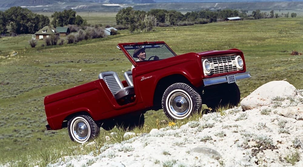 A red 1966 Ford Bronco Roadster is shown being driven up a hill off-road.