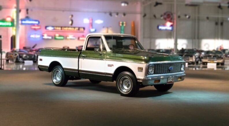 A green and white 1971 Chevrolet C-10 Pickup is shown on a showroom floor near a used truck dealer.