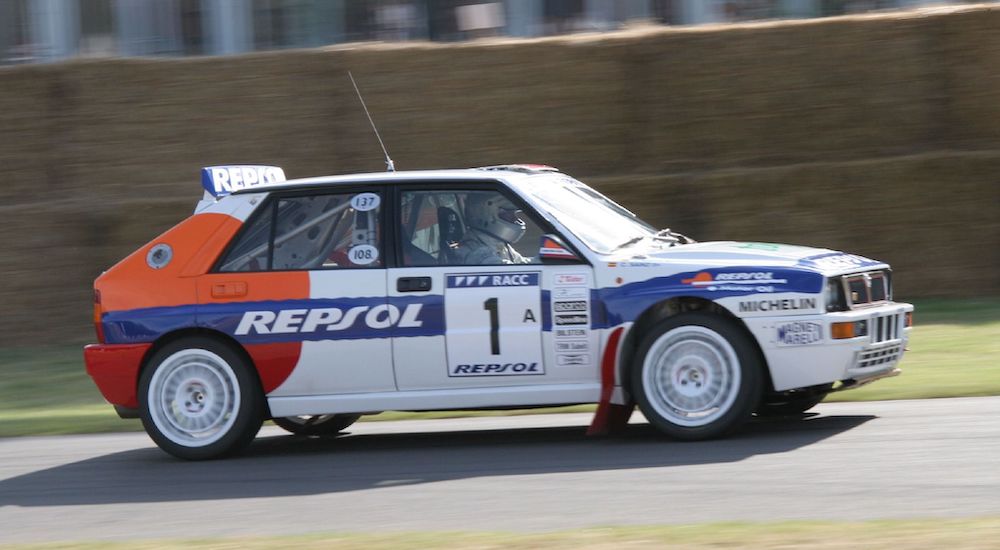 A white 1993 Lancia Delta HF integrale is shown racing at a rally.