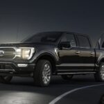 A black 2023 Ford F-150 Lariat Limited is shown towing a trailer at night.