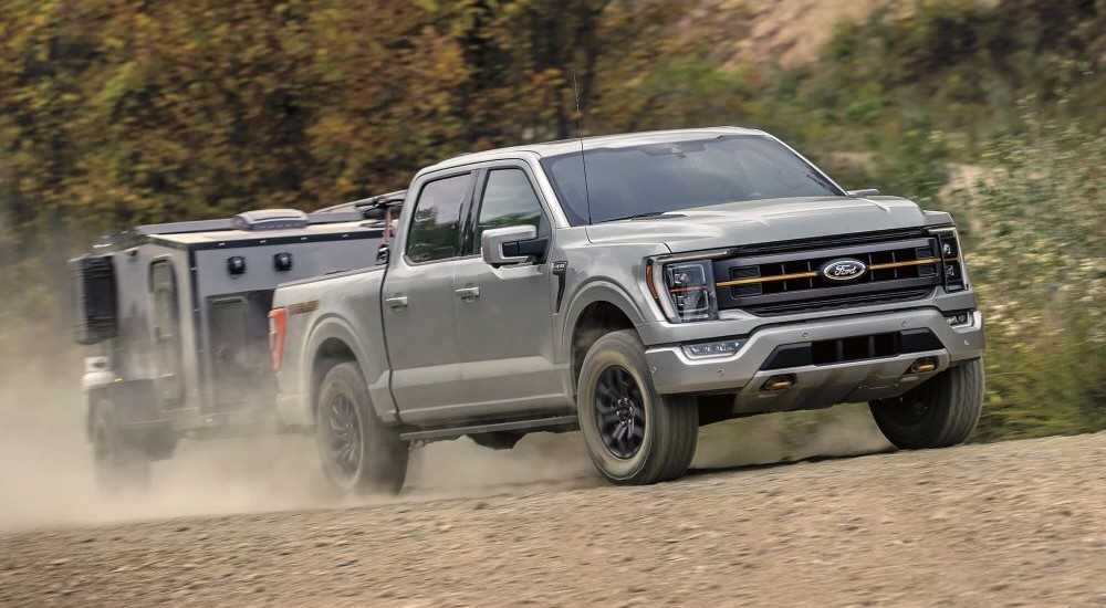 A silver 2023 Ford F-150 Tremor is shown towing a trailer off-road.