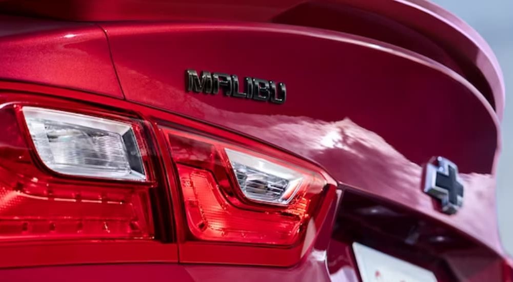 A close-up of a red 2024 Chevy Malibu badge is shown. 