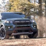 A new Ford explorer for sale, a green 2024 Ford Explorer Timberline, is shown driving in a forest.