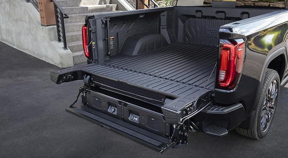 The open tailgate of a black 2024 GMC Sierra 1500 Denali is shown parked near stairs.