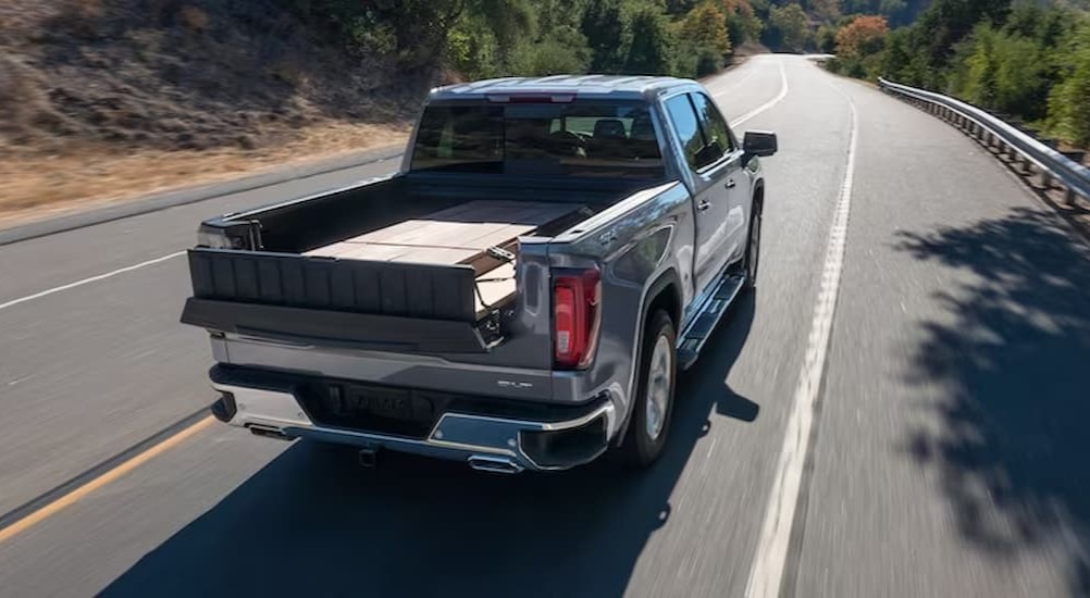 A gray 2024 GMC Sierra 1500 SLT is shown driving on a highway.