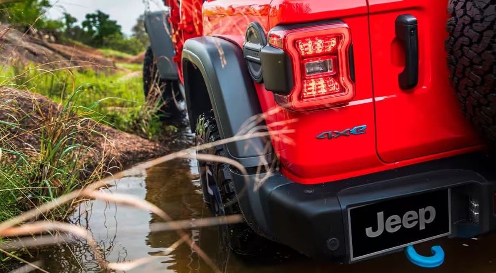 A red 2024 Jeep Wrangler 4xe is shown in a close-up of its rear side while driving through a puddle.