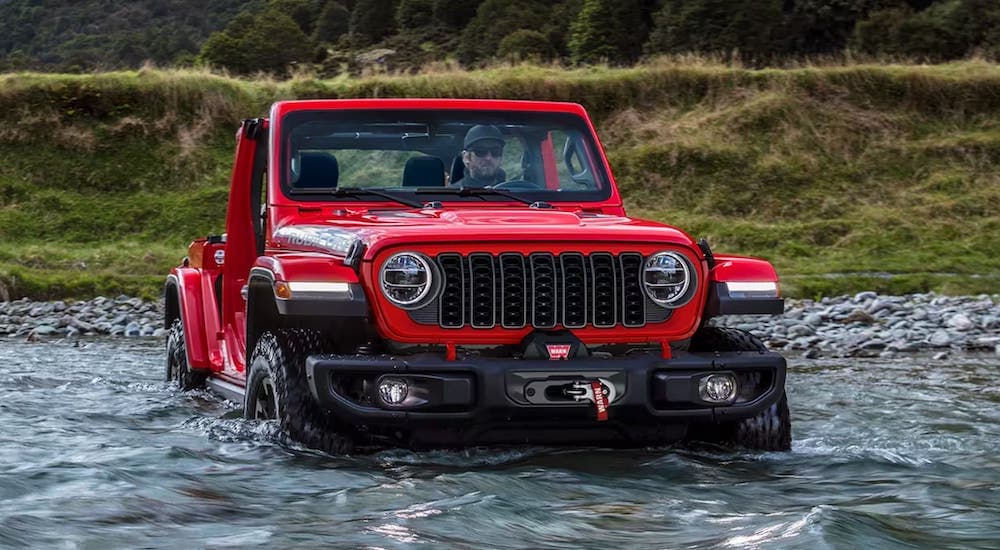 A red 2024 Jeep Wrangler is shown fording a river.
