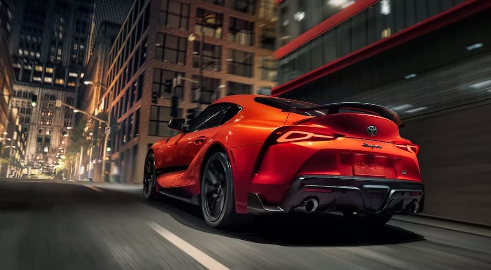 A bright orange 2024 Toyota GR Supra is shown driving through a city at night.