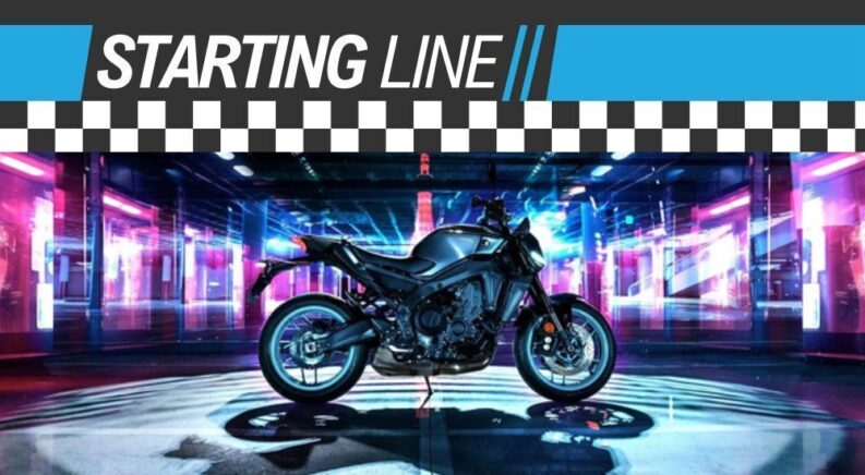A black and blue 2024 Yamaha MT-09 is shown parked near neon lights under a Starting Line banner.