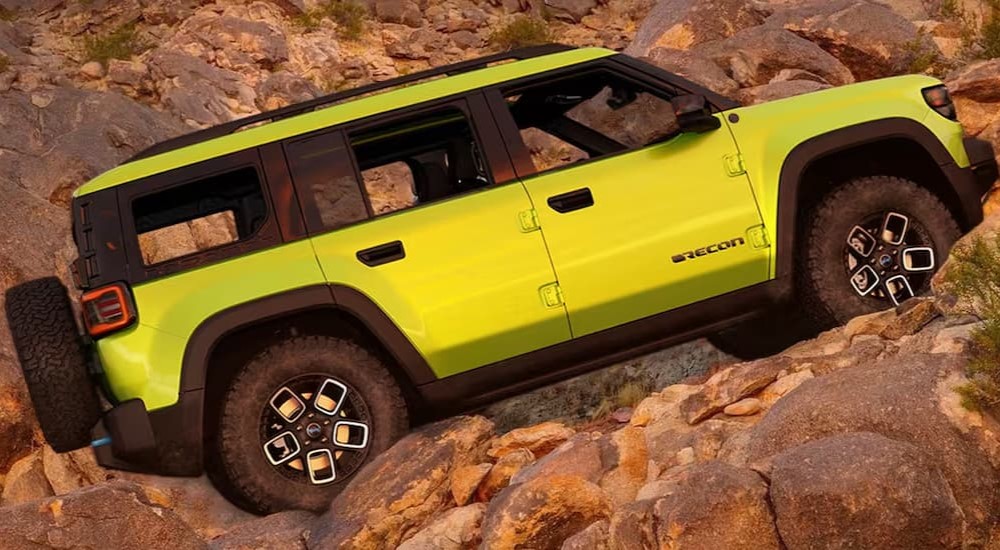 A green 2025 Jeep Recon is shown driving off-road on a rocky path.