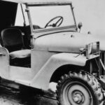 A black-and-white photograph of a 1940 Willys Quad is shown parked at an old used Jeep dealership.