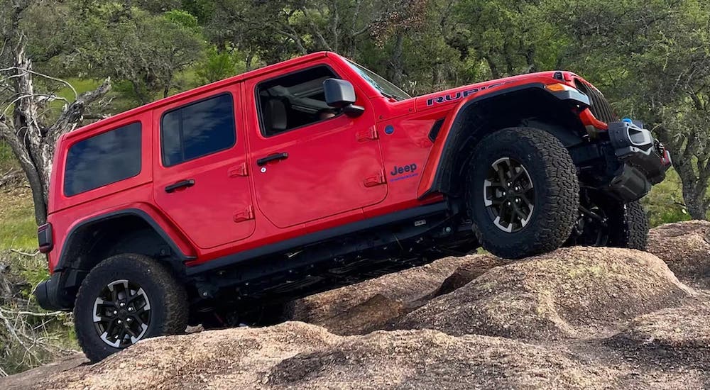 A red 2024 Jeep Wrangler Rubicon is shown driving off-road and up a hill.