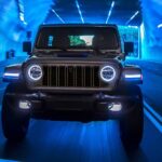 A black 2024 Jeep Wrangler is shown driving from a Jeep dealer in a lit tunnel.