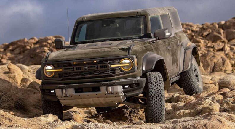 One of the most popular Ford SUVs for sale, a green 2024 Ford Bronco Raptor, is shown driving off-road through a desert.